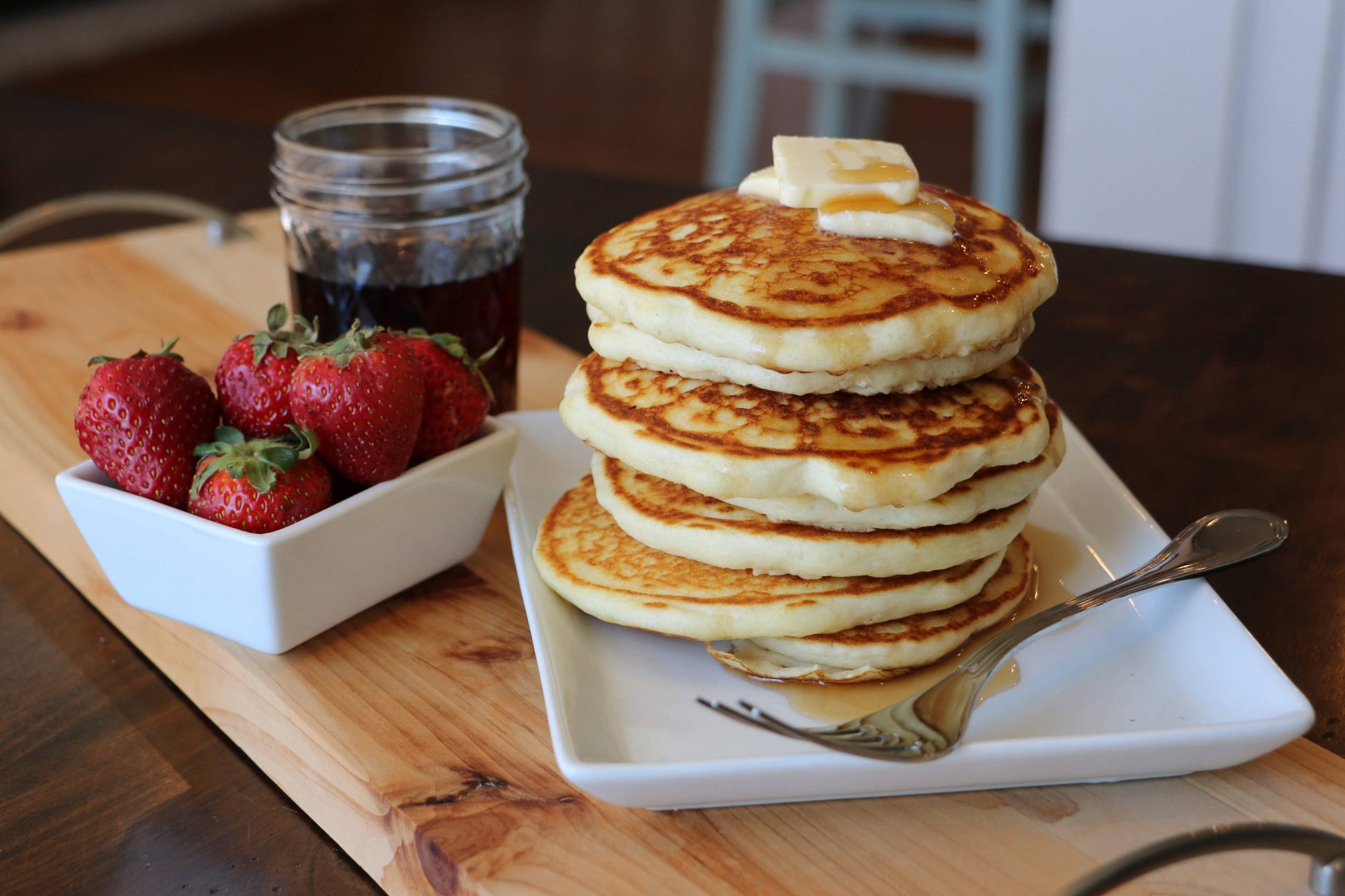 Stack of pancakes with syrup and strawberries on a wooden table