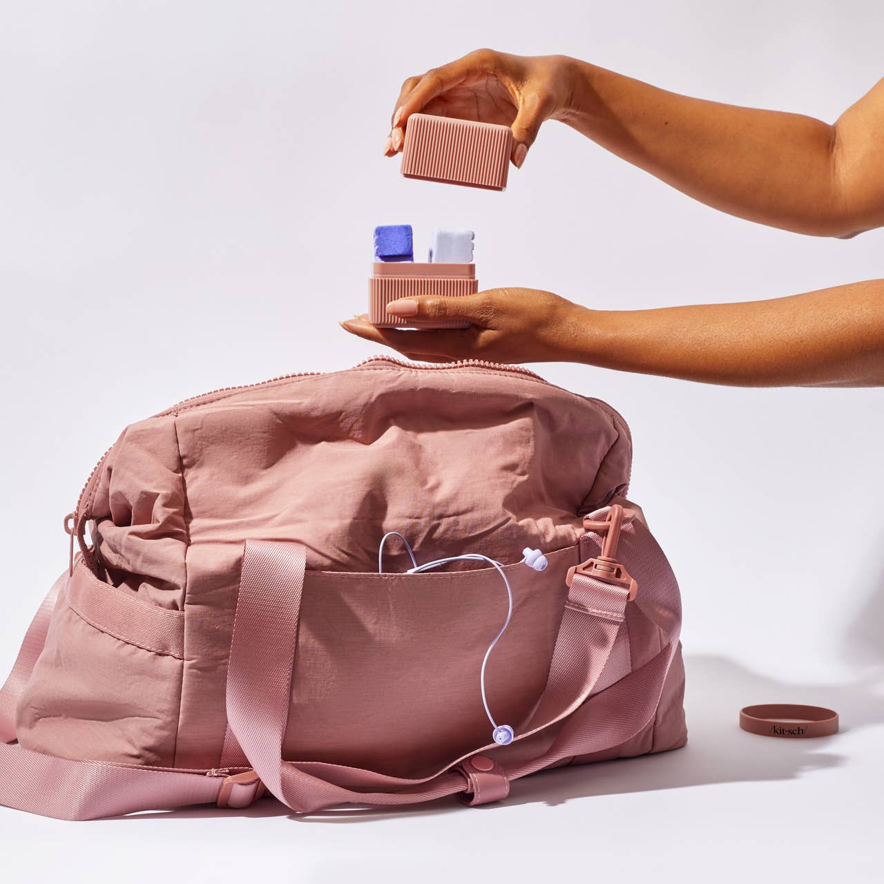 Person organizing items into a pink bag on a white background
