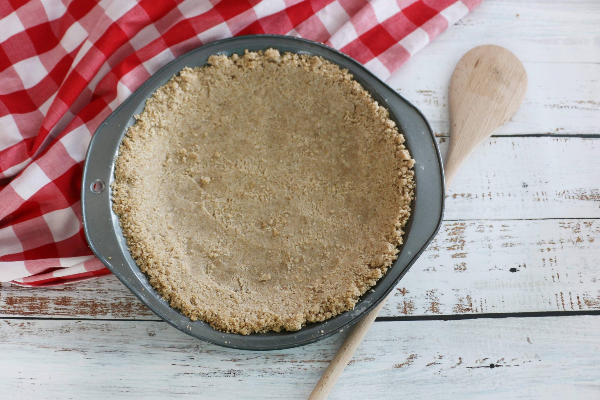 Pie crust in a pan on a wooden surface with a checkered cloth