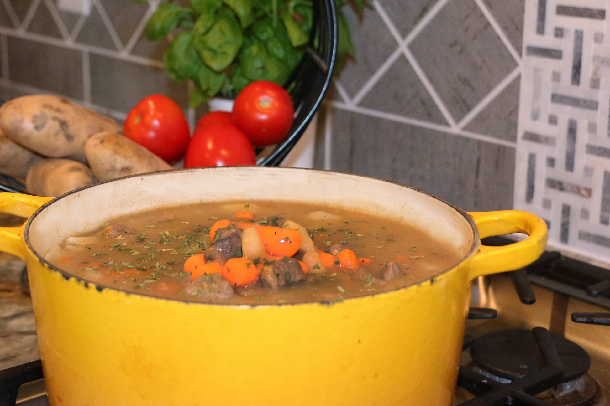 Yellow pot of soup on a stove with vegetables and bread in the background