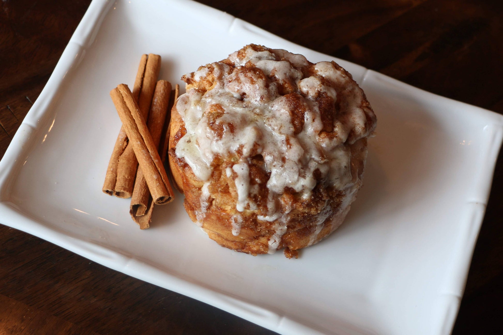 Cinnamon roll with icing on a white plate with cinnamon sticks