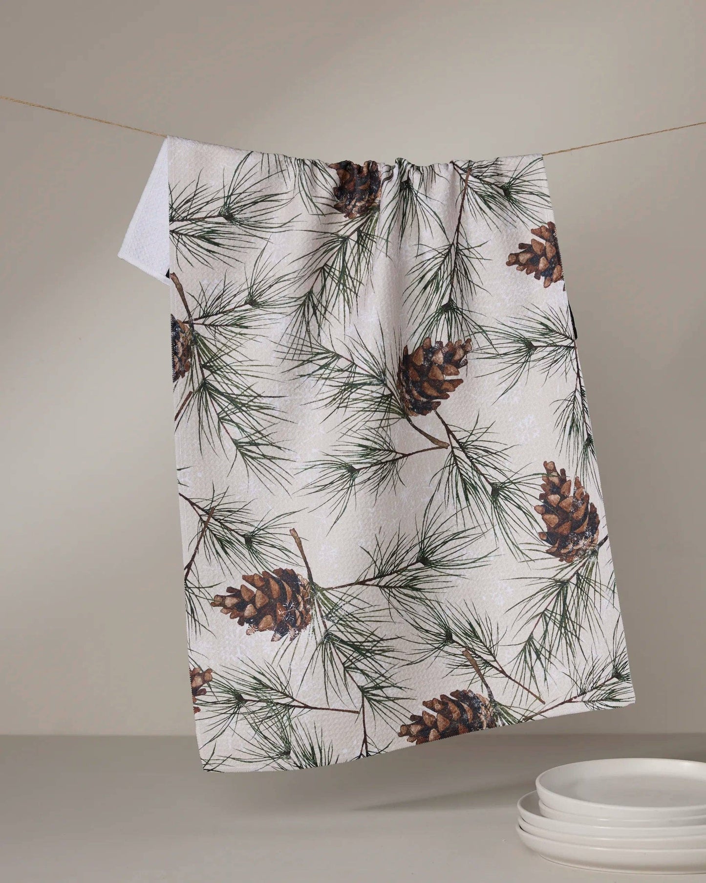 Geometry Tea Towel Evergreen Frost  Towel with pine cone and branch pattern hanging on a line against a neutral background