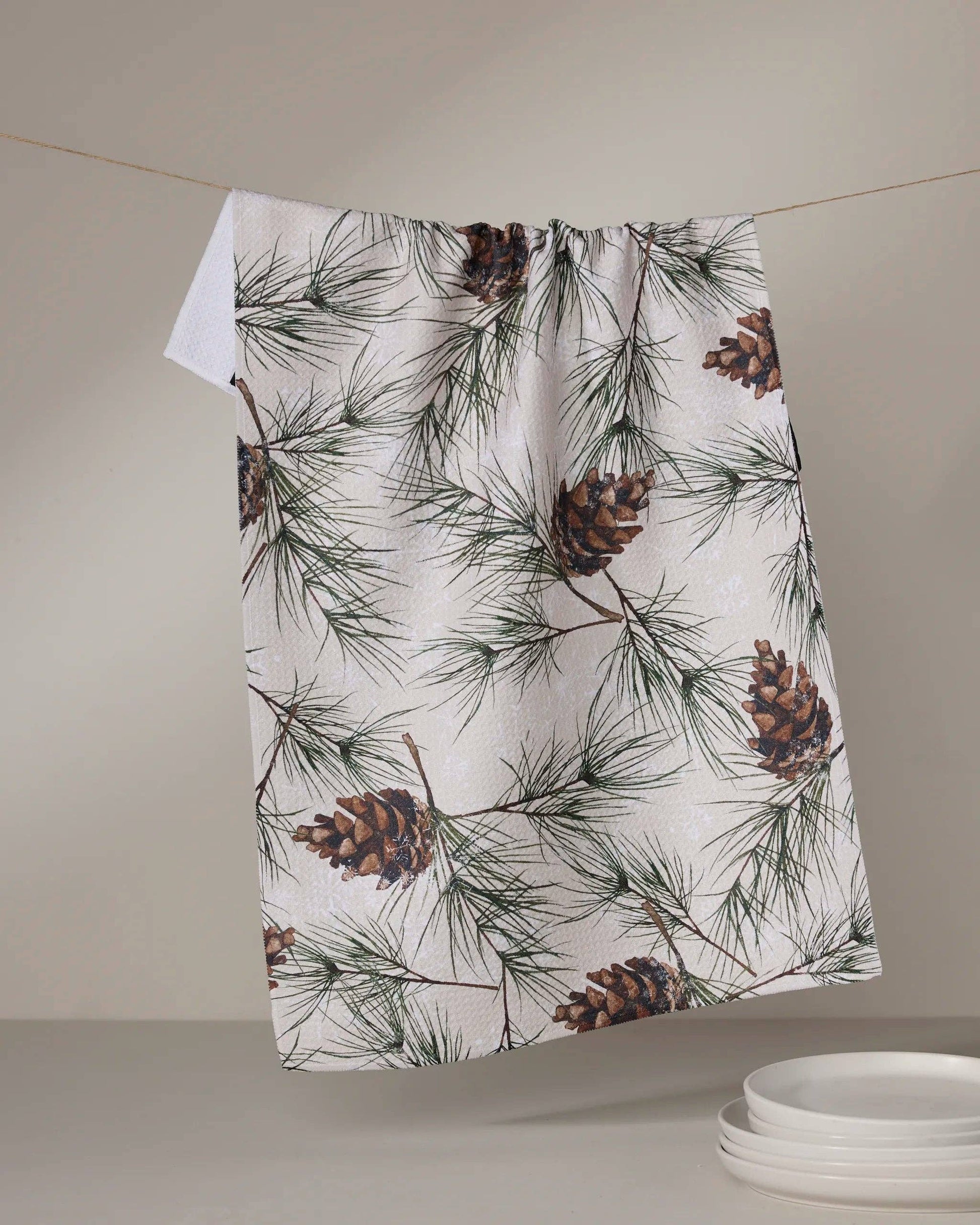 Geometry Tea Towel Evergreen Frost  Towel with pine cone and branch pattern hanging on a line against a neutral background
