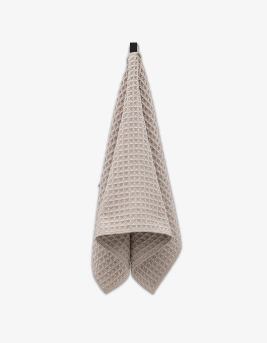 A taupe waffle hand towel hanging against a white background.