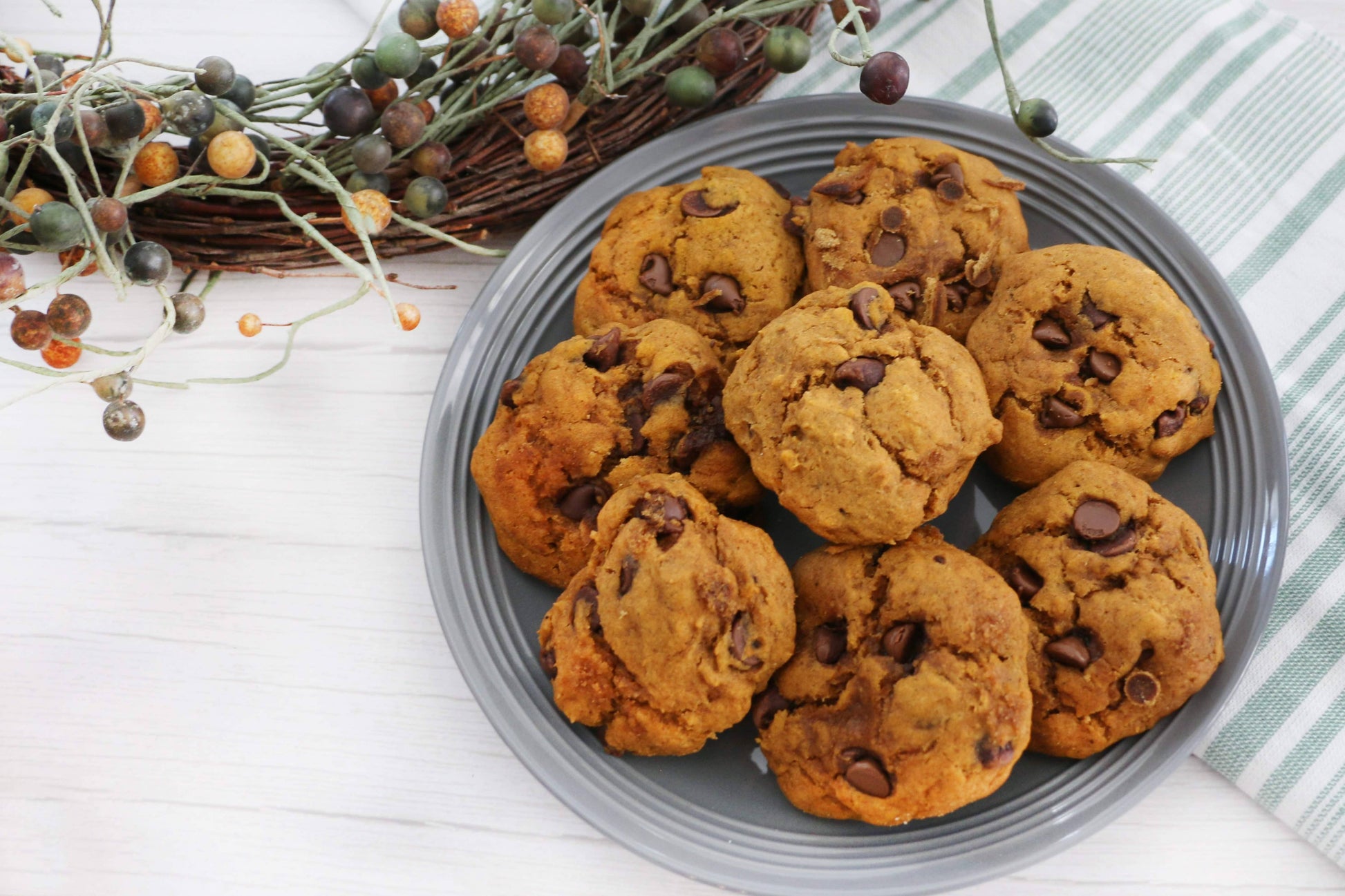 Plate of pumpkin chocolate chip cookies on a white wooden surface with decorative elements.