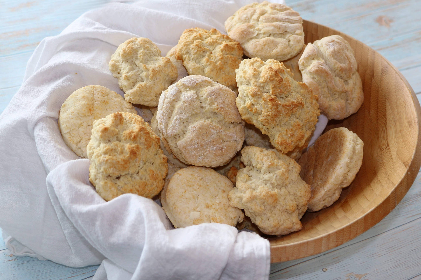 Wooden bowl filled with freshly baked biscuits on a light blue surface.