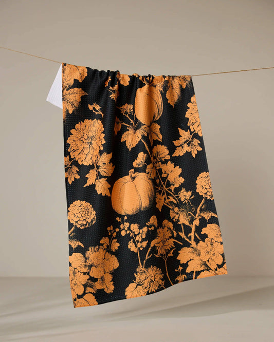 Black Geometry brand kitchen tea towel with orange floral and pumpkin pattern on a beige background