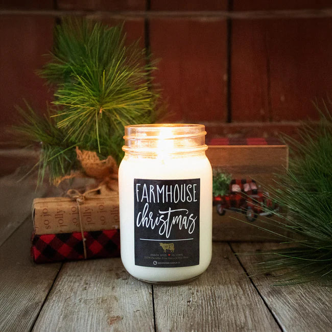 Candle in a jar labeled 'Farmhouse Christmas' on a wooden surface with decorative elements.