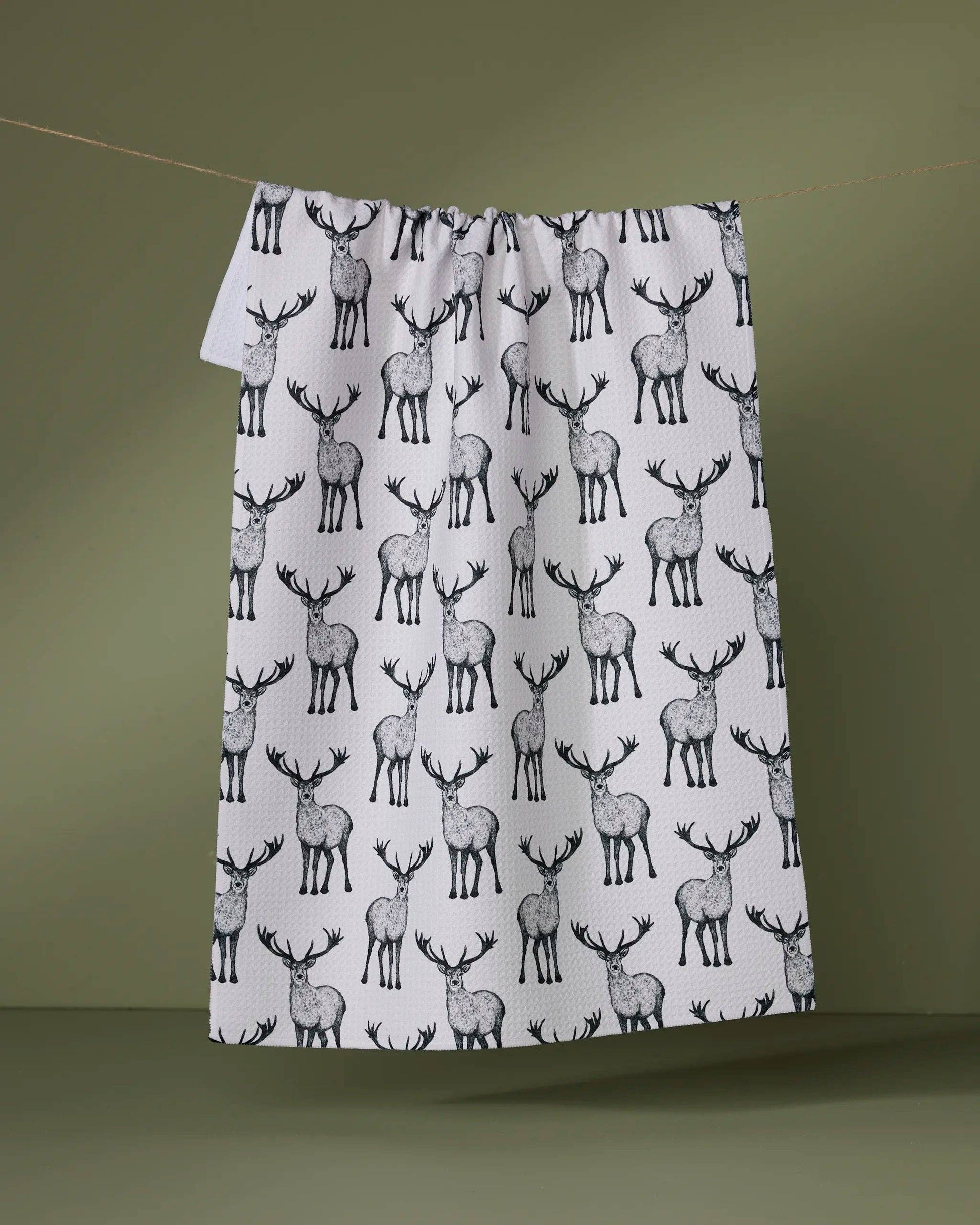 Geometry Tea Towel with deer pattern hanging on a line against a green background