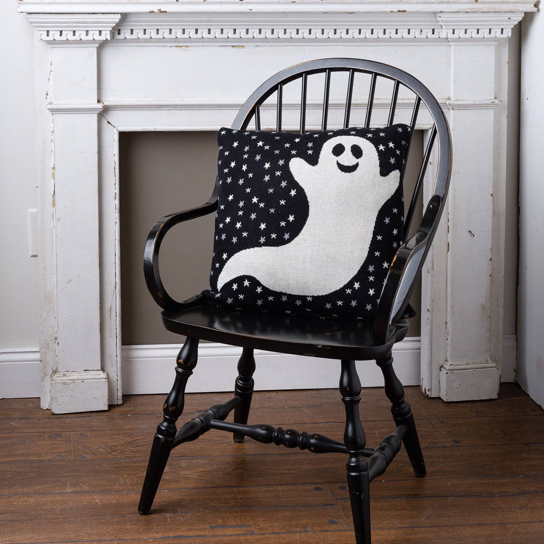Black armchair with a pillow featuring a ghost design in front of a white fireplace.