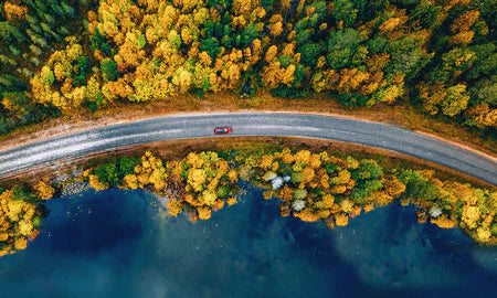 Aerial view of a winding road surrounded by autumn-colored trees and a lake.