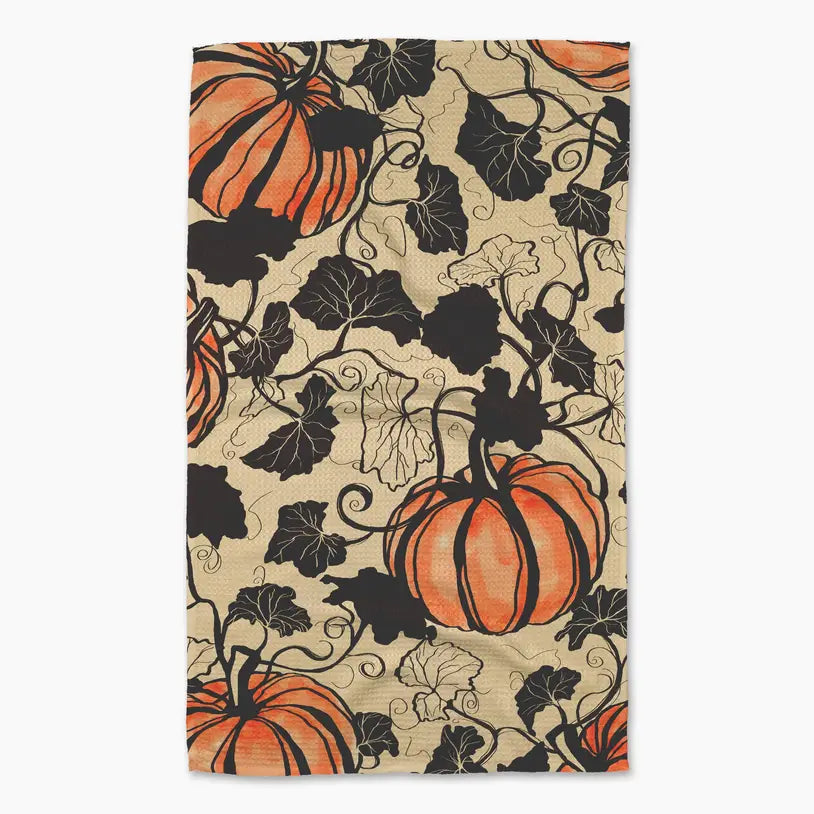 A Geometry  tea towel featuring a repeating autumn pattern of orange pumpkins and black vines on a warm beige background.