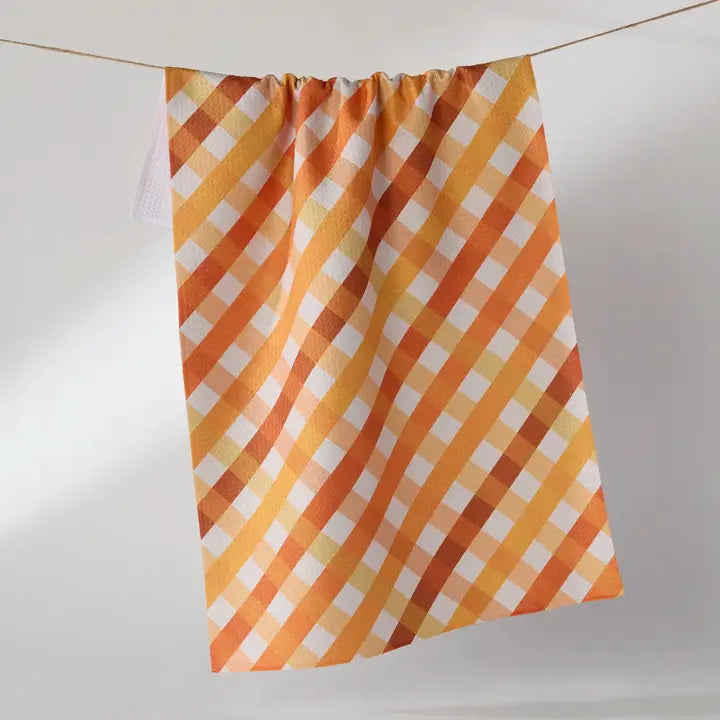 A kitchen towel with a diagonal gingham pattern in orange, yellow, and white, hanging from a string against a plain light gray background.