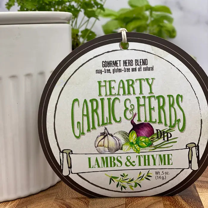 Label for 'Hearty Garlic & Herbs Dip' by Lambs & Thyme on a wooden surface with plants in the background.