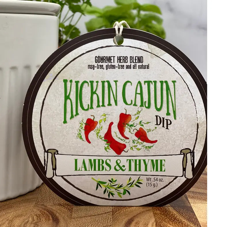Round label for 'Kickin Cajun Dip' by Lambs & Thyme on a wooden surface with a blurred background.