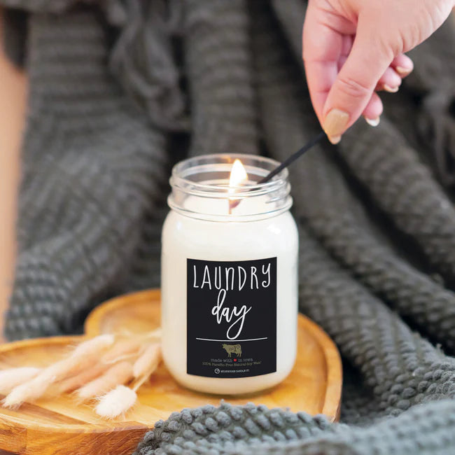 Candle labeled 'Laundry Day' being lit with a wooden coaster and laundry-themed decor in the background.