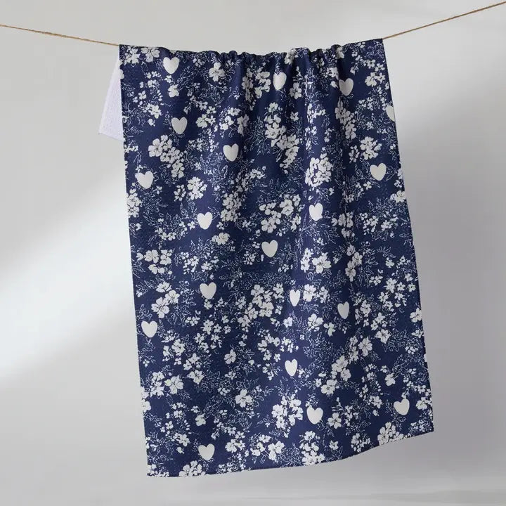 A navy blue kitchen towel with a white floral and heart pattern, hanging from a string against a plain light gray background.