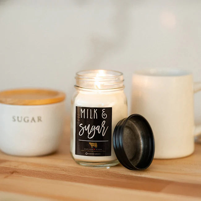 Candle labeled 'Milk & Sugar' on a wooden surface with mugs in the background