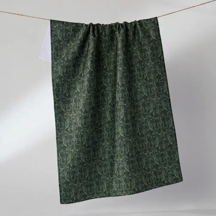 A dark green Geometry tea towel with an intricate repeating damask pattern, hanging from a thin string against a plain light gray background.