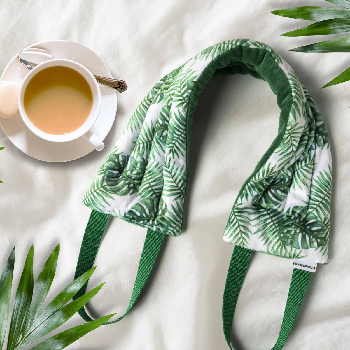 Green leaf-patterned headband on a white surface with a cup of tea and leaves.