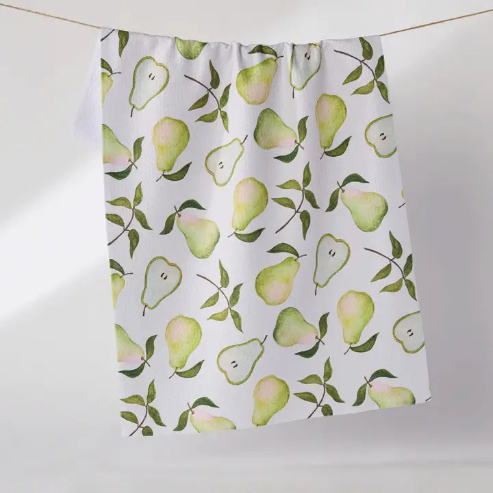 A white Geometry tea towel featuring a repeating watercolor pattern of green pears and leaves, hanging from a metal rod against a light gray wall.