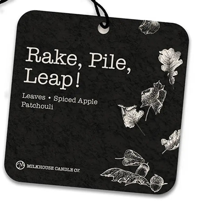 A square black air freshner with rounded corners, hanging from a black string. White text reads 'Rake, Pile, Leap!' and 'Leaves • Spiced Apple Patchouli,' with white leaf illustrations scattered on a dark textured background.
