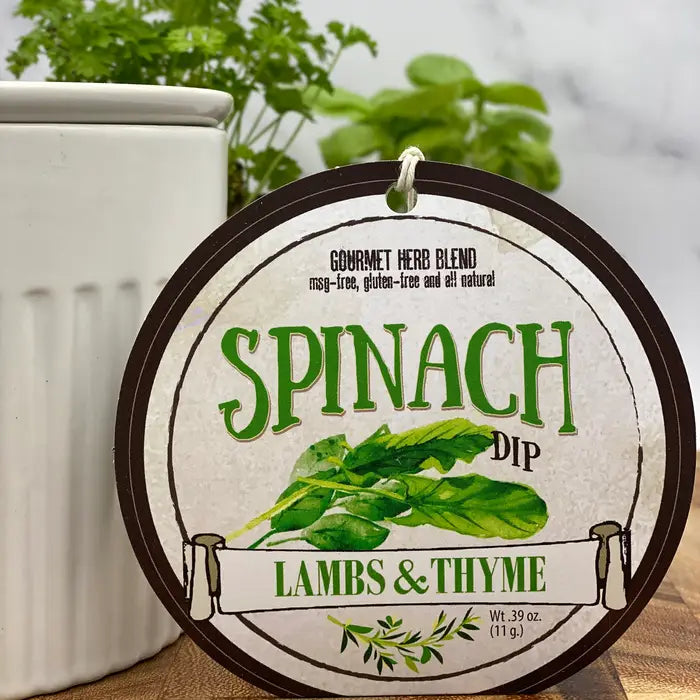Label for spinach dip by Lambs & Thyme on a wooden surface with a plant in the background.