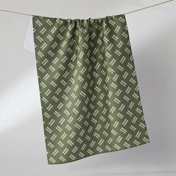 An olive green Geometry tea towel with a repeating white geometric pattern, hanging from a thin cord against a light gray background.